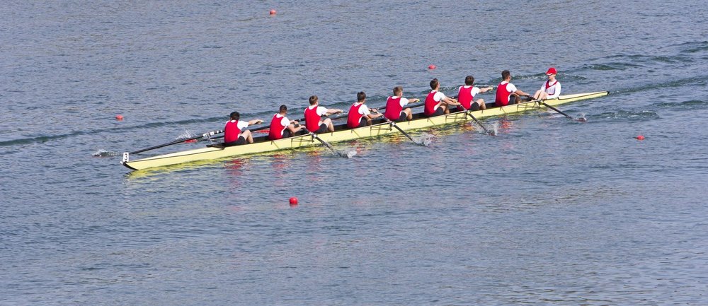Ein Achter-Ruderboot mit acht synchron rudernden Teammitgliedern und Steuermann als Symbol für agile Zusammenarbeit, klare Führung und erfolgreiche Transformation im Banking.